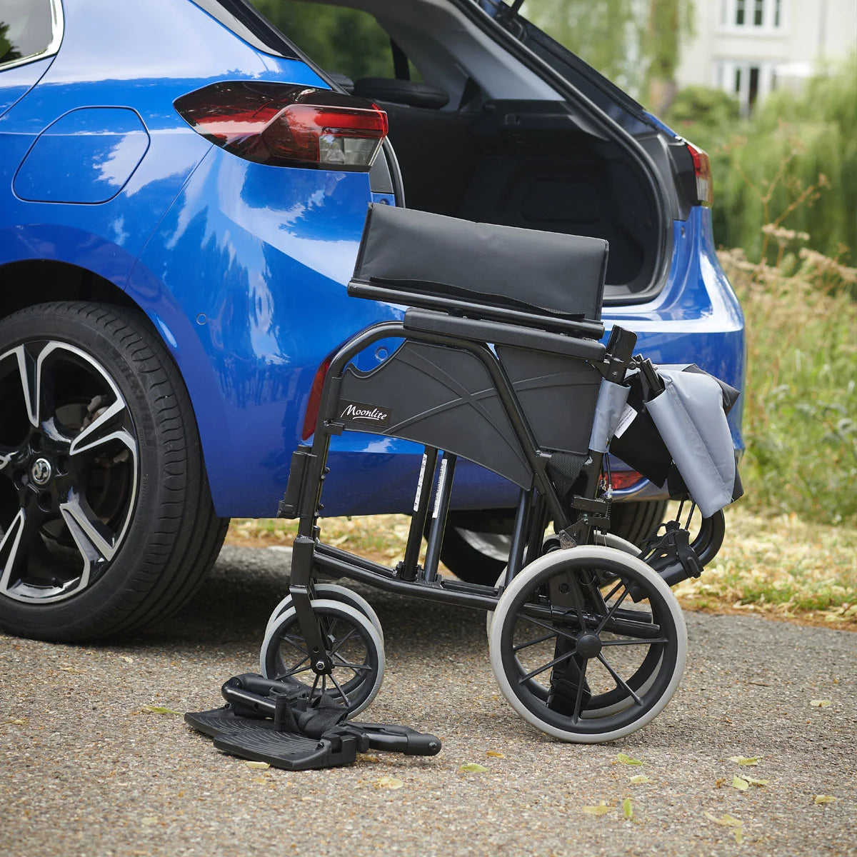 Black breezy manual wheelchair next to a blue car with grass and a house in the background