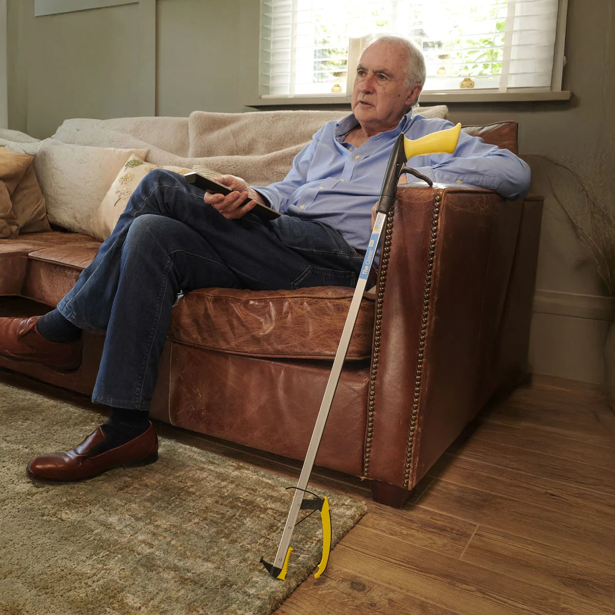 Man sitting on a brown leather couch with a with a  pair of tongs in a living room.