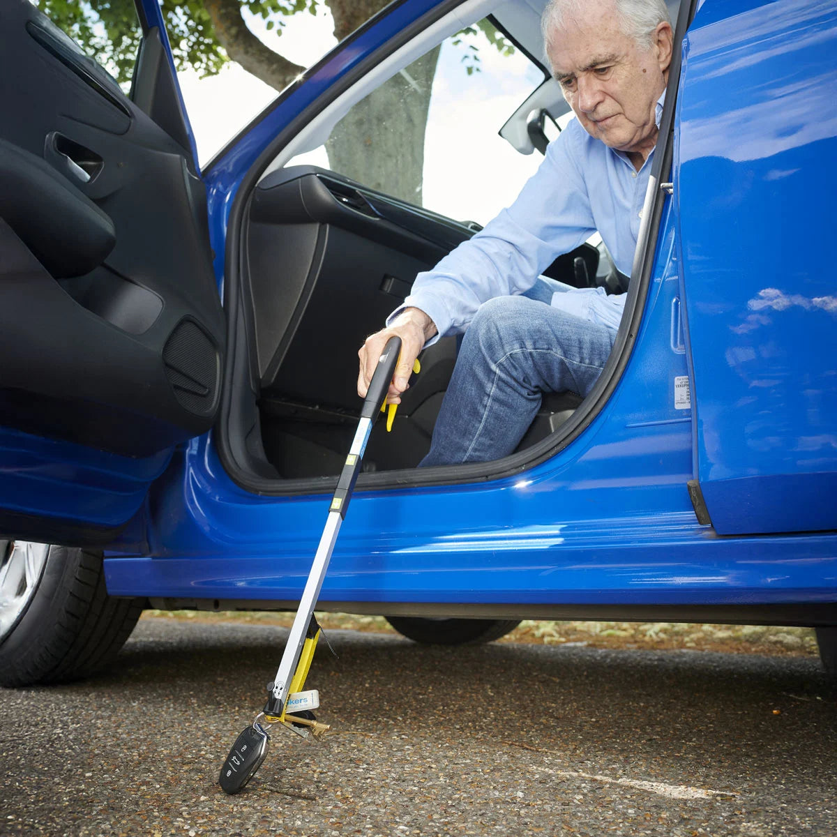 A man using a pair of tongs to reach car keys dropped on the floor
