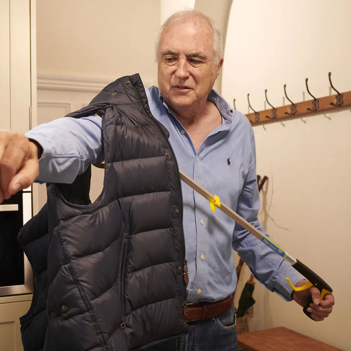 A man is using a pair of tongs to help him put on a black vest