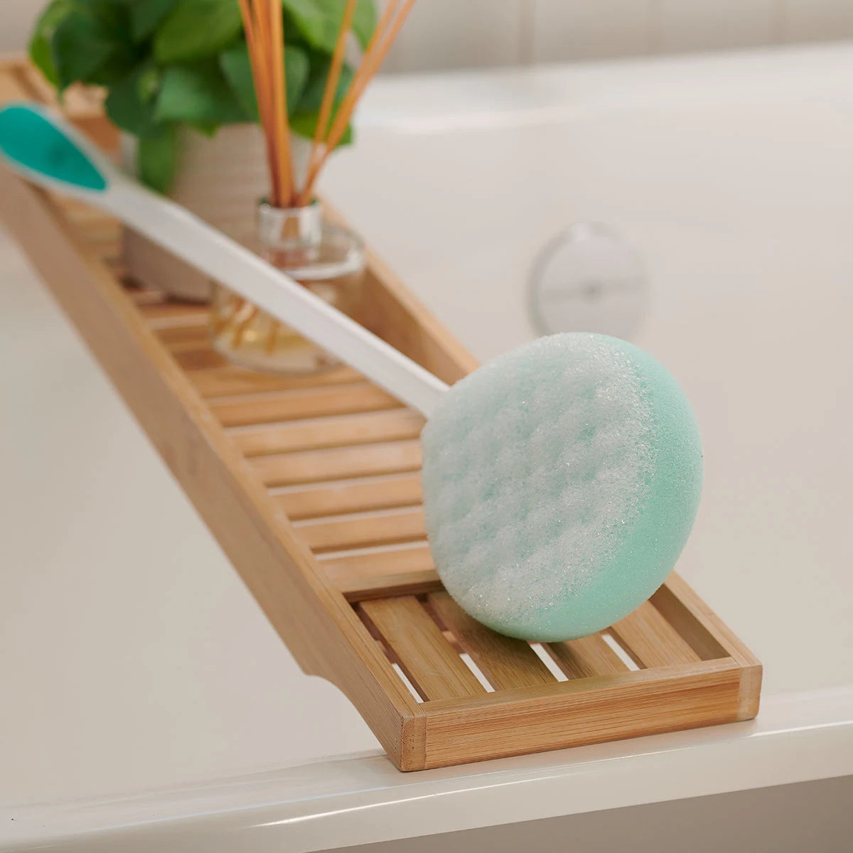 Bath brush with a green sponge head on a wooden tray in a bathroom setting.