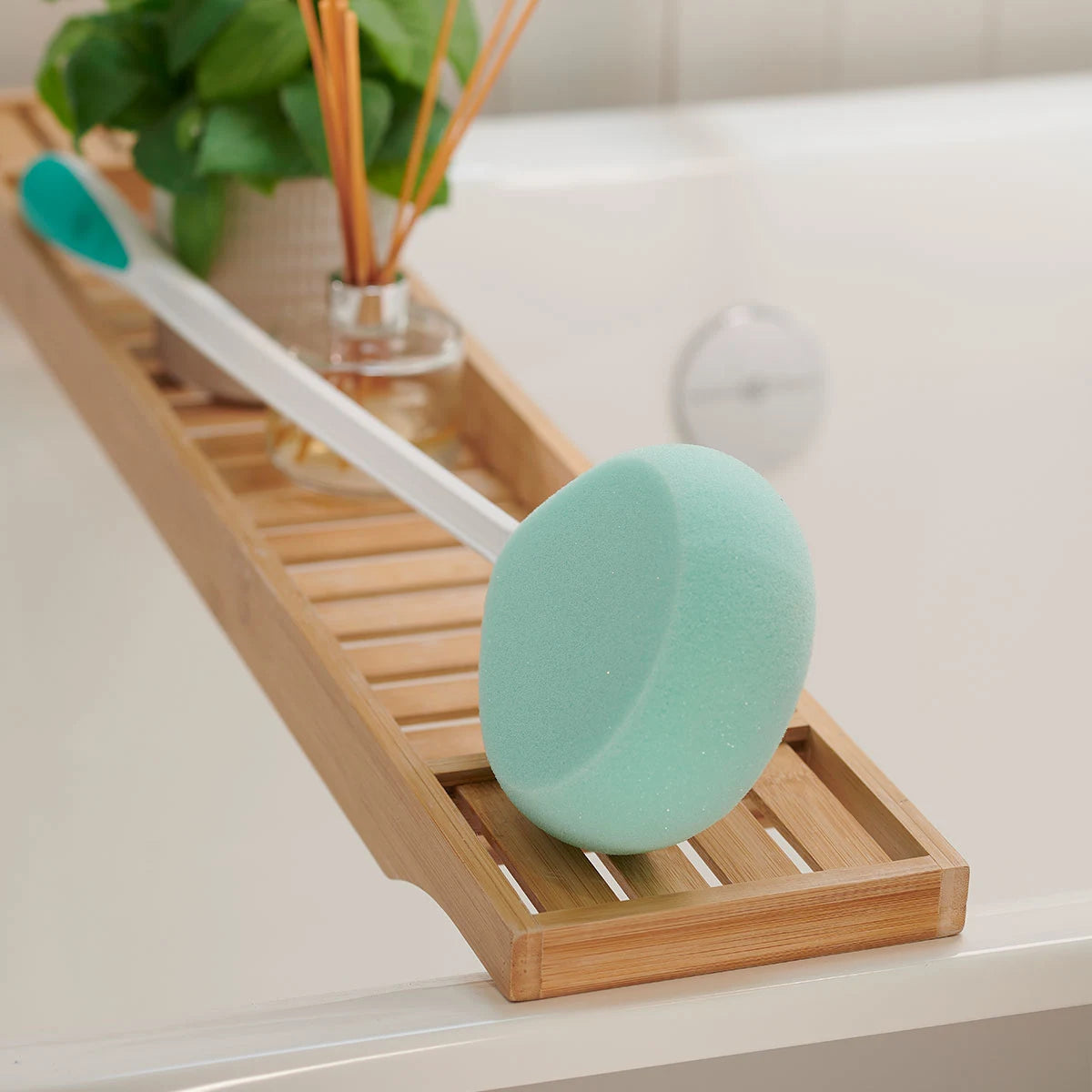 Green bath sponge on a wooden tray with a plant in the background