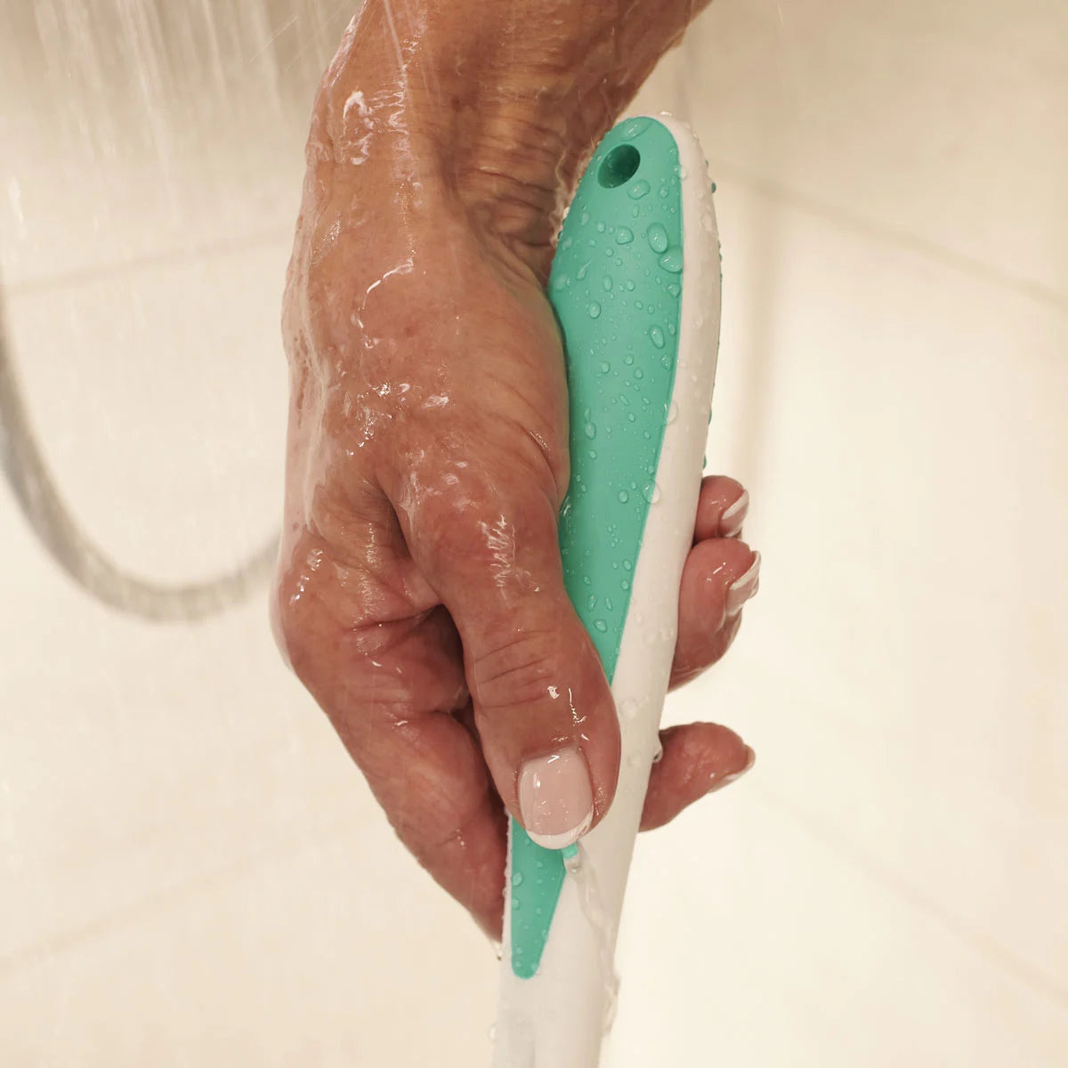 Hand holding a green and white shower sponge with water droplets on a neutral background