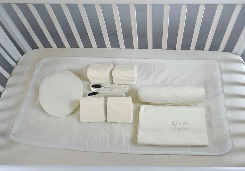 Collection of baby care items on a crib mattress with a gray and white striped crib in the background.
