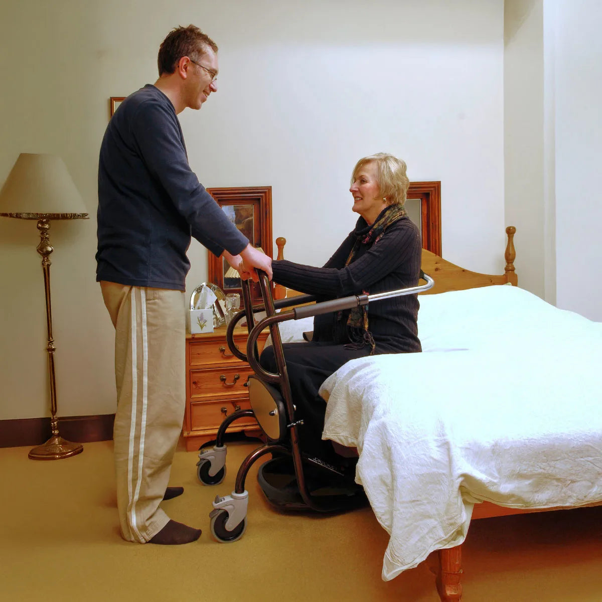 Man supporting woman in cricket transfer aid walking frame.
