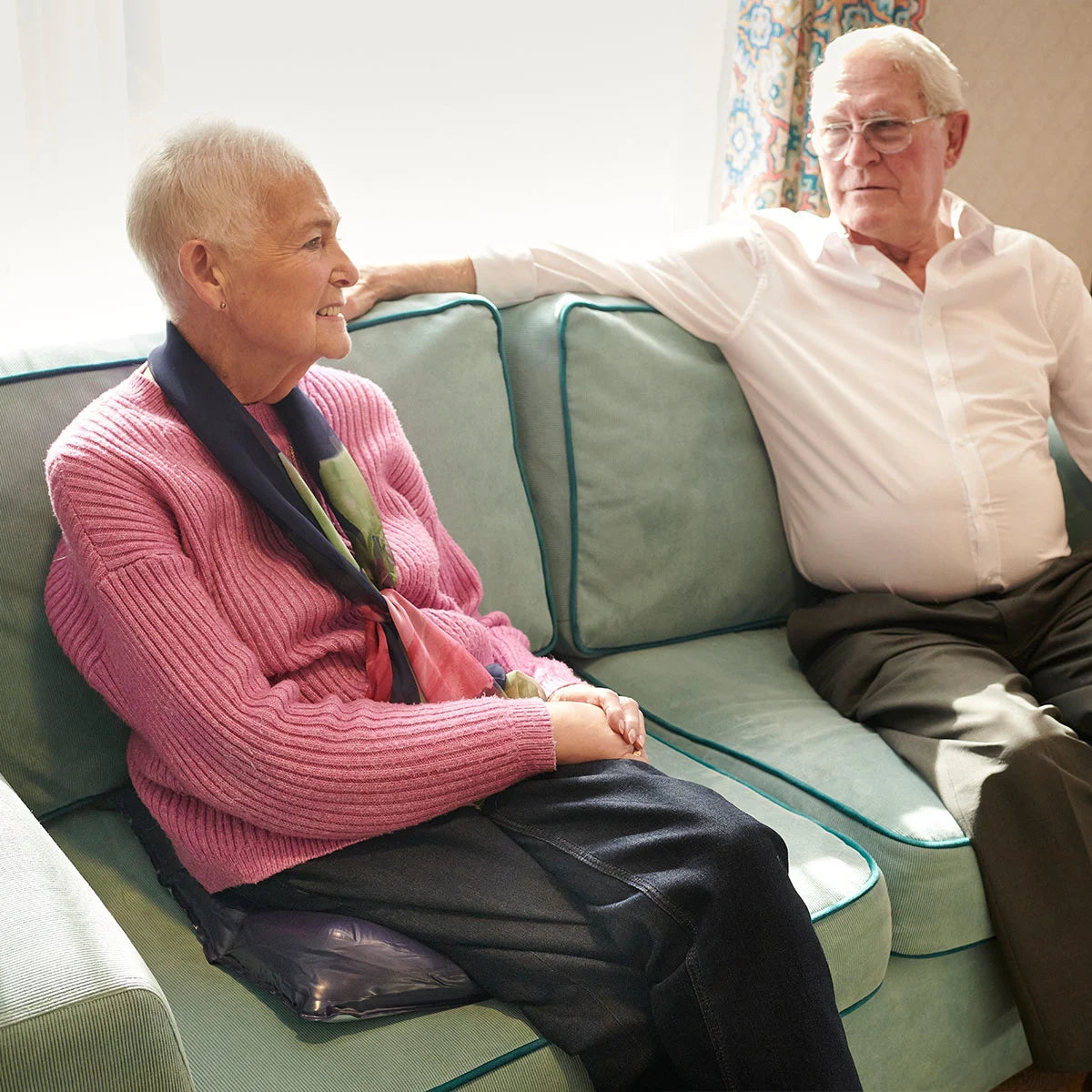 Two elderly people sitting together, one sitting on a JAY EquaZone Air wheelchair cushion.