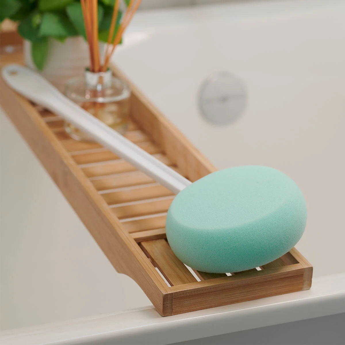 Bathroom scene with a wooden tray holding a green bath sponge.