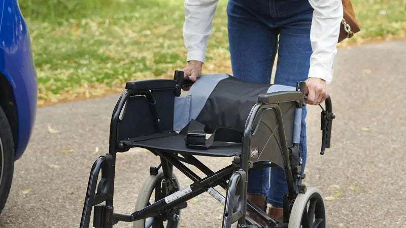 Person pushing a folded wheelchair on a paved path