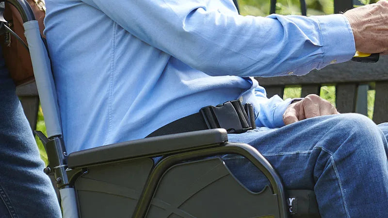Person sitting in a wheelchair with a blue shirt and jeans that has been strapped in.