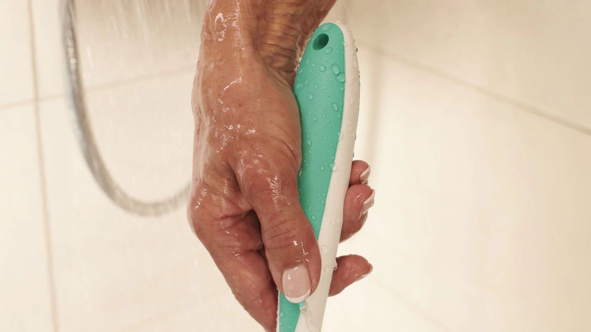 Hand holding a teal and white bath brush against a tiled bathroom background