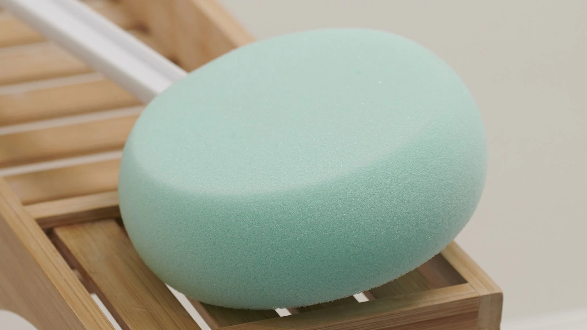 Green bath sponge on a wooden bath caddy with a white background