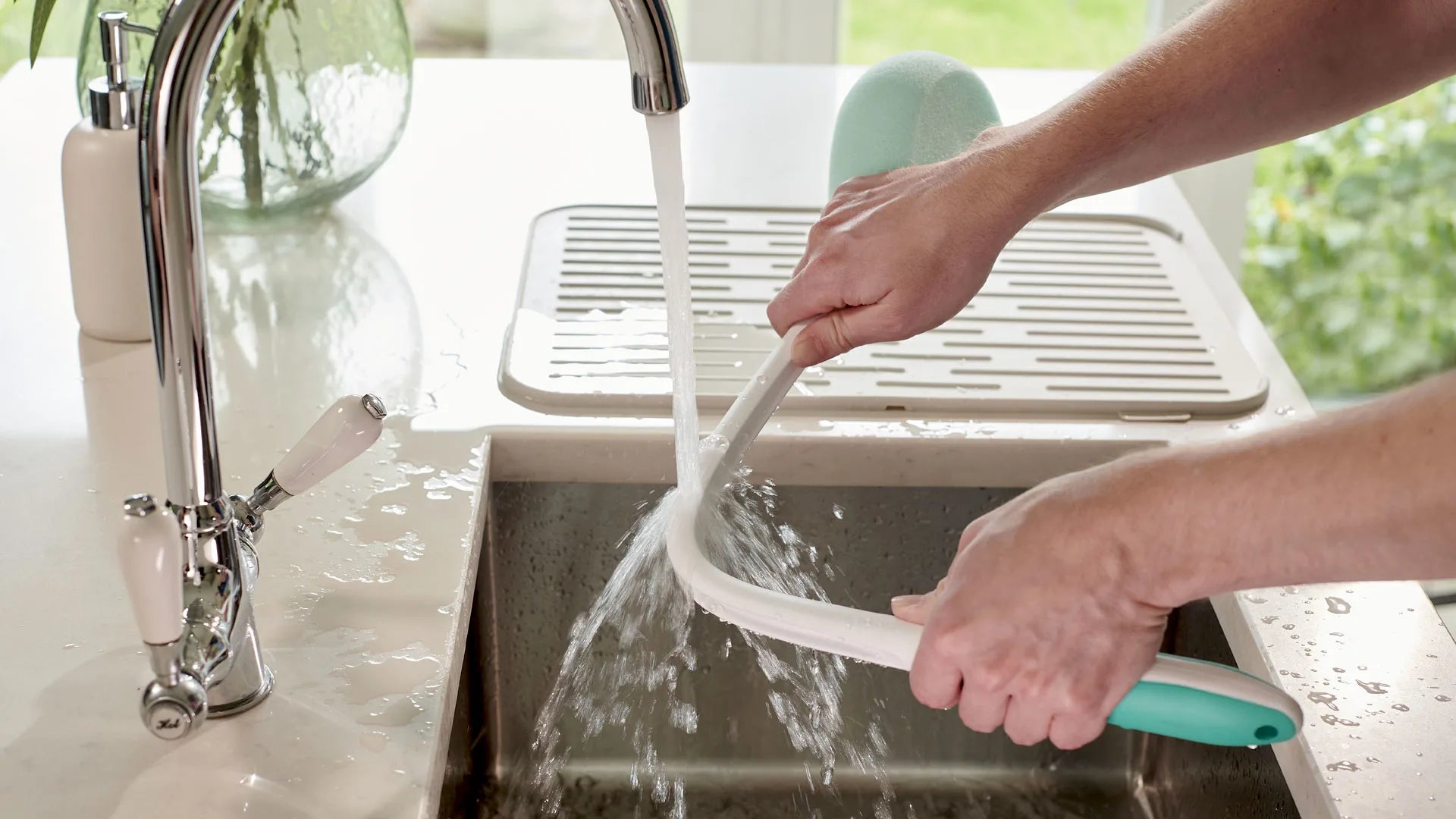 Person washing a white bath sponge in a kitchen sink with running water.
