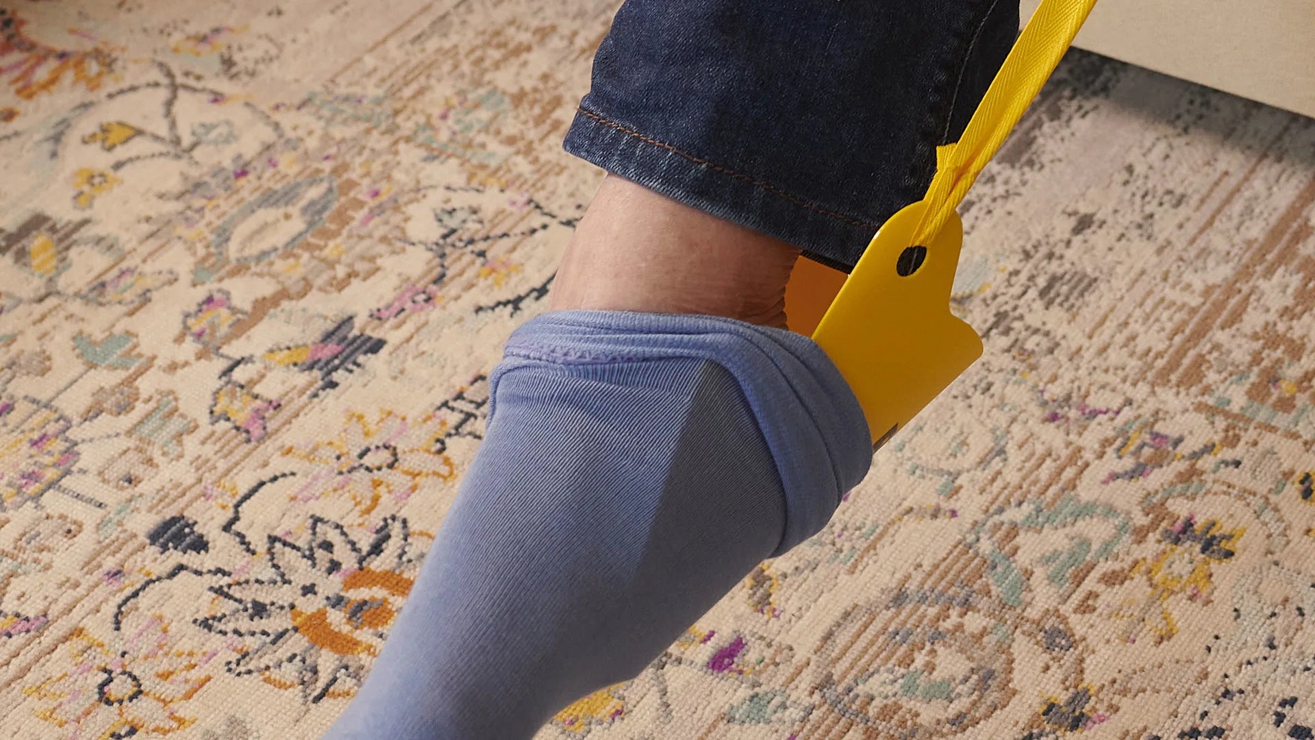 Person using a yellow sock aid to put on blue socks
