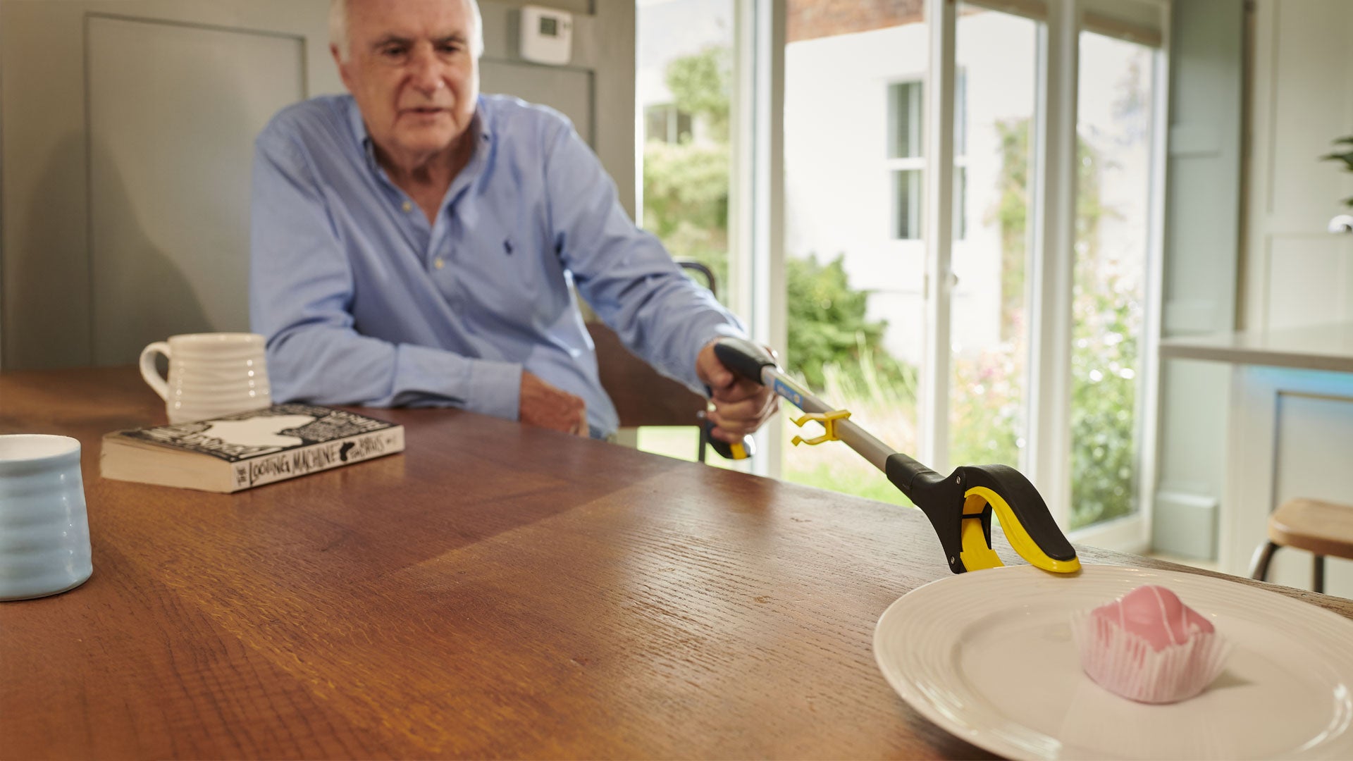 A man using the handi grip to grab a plate with a pink cake on it