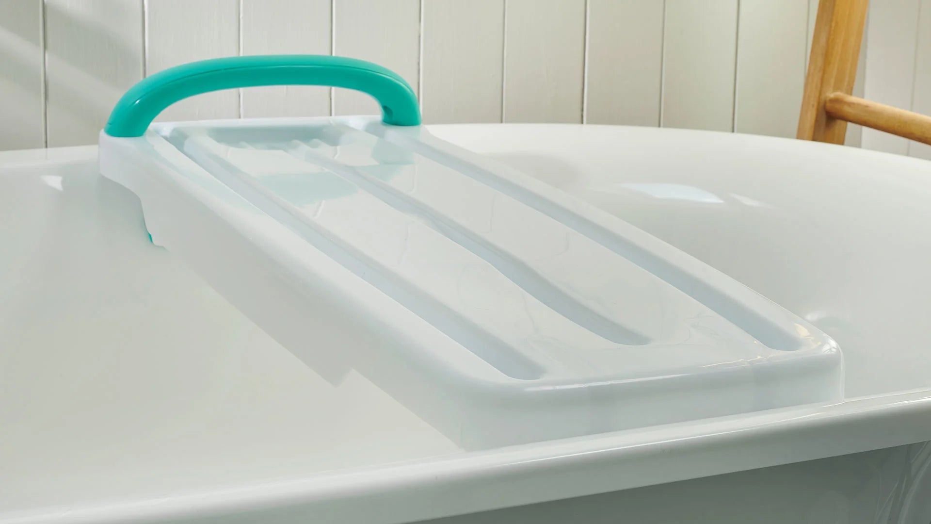 White bathtub with a green handle with a white bathroom caddy against a white tiled wall