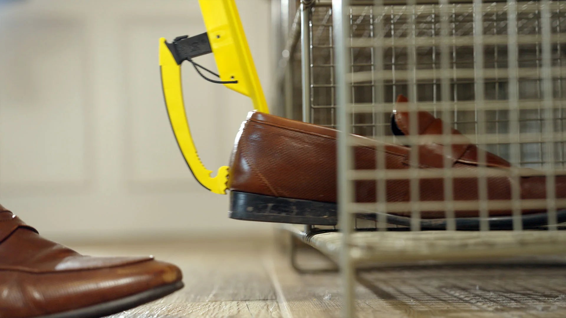 Brown shoes being grabbed by a yellow shoe helper with a blurred background