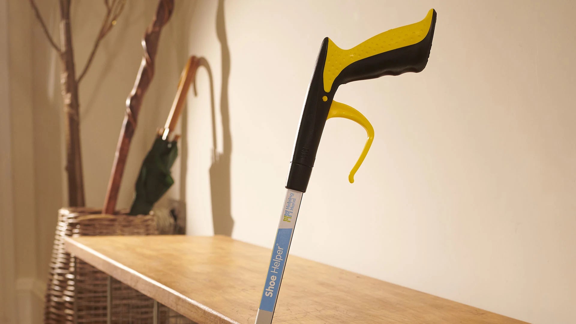 Shoe helper with black and yellow handle on a wooden surface against a beige wall.