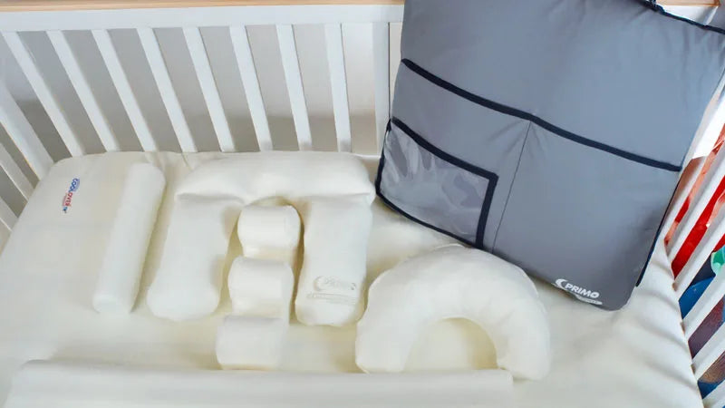 Baby crib with white mattress, gray pillow, and colorful blanket