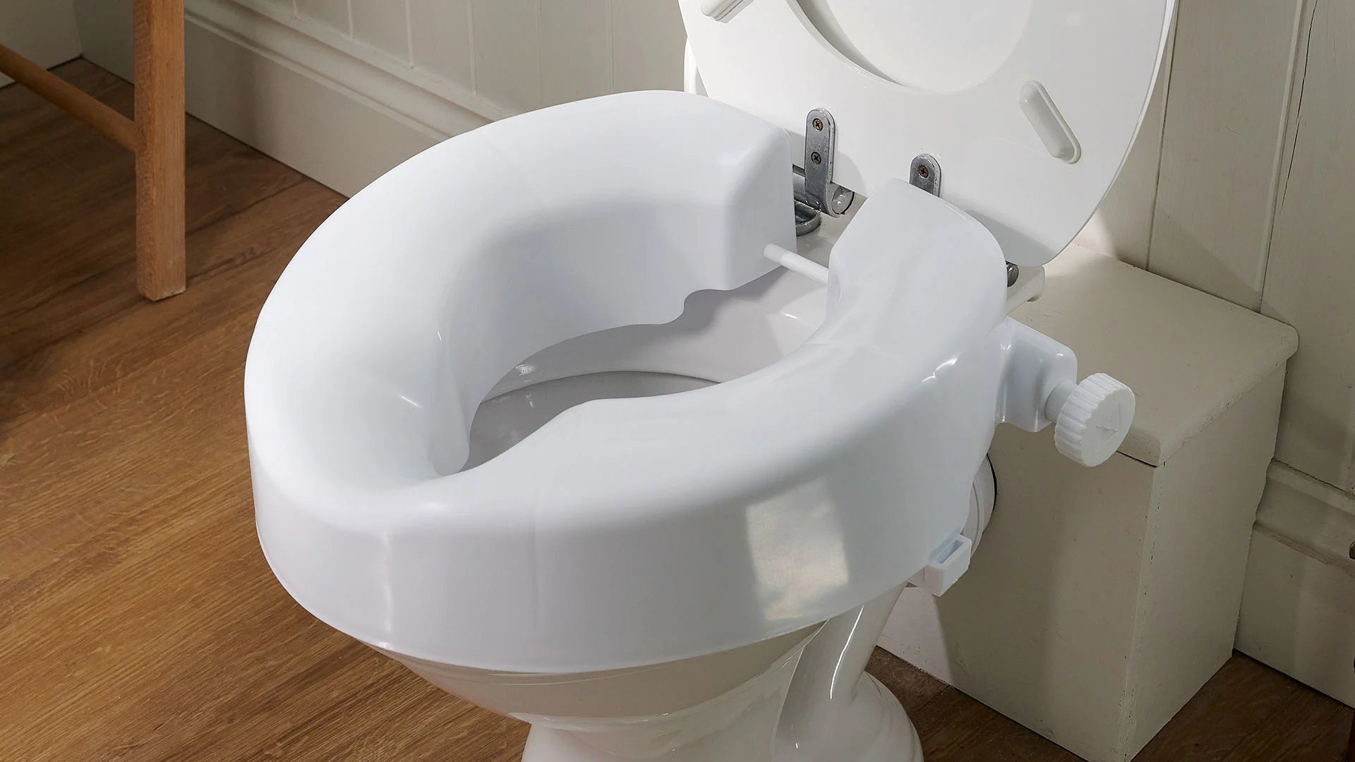 White toilet seat with a raised rim on a wooden floor.