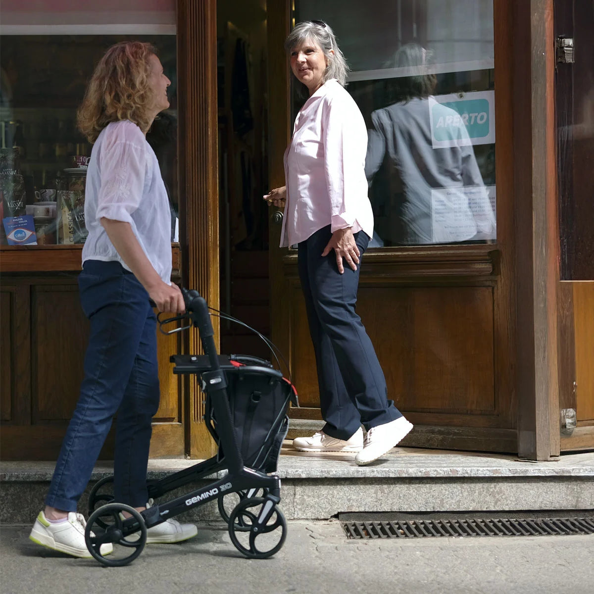 Two Women interacting outside a shop with Lightweight Gemino 30 Carbon Rollator.