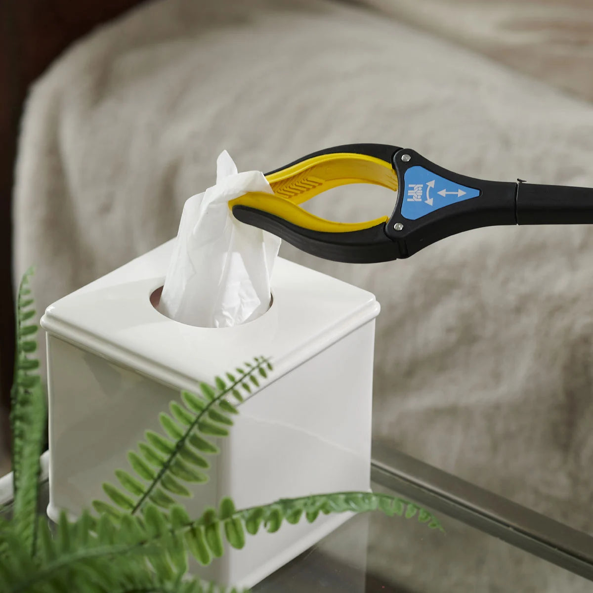 Tissue paper being pulled from a box with a handi grip pro, next to a plant.