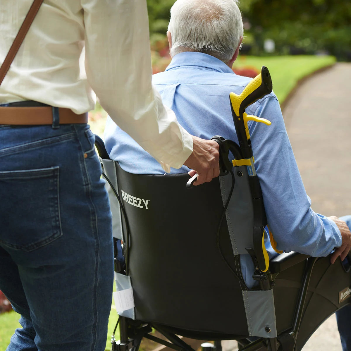 A person pushing someone in a wheel chair that has a mini reacher clipped on to it