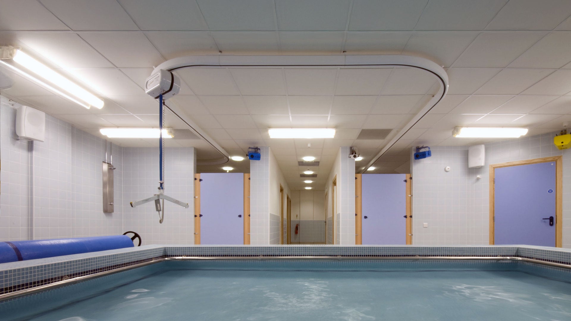 Skyframe hoist poser mounted on ceiling above indoor therapy pool.