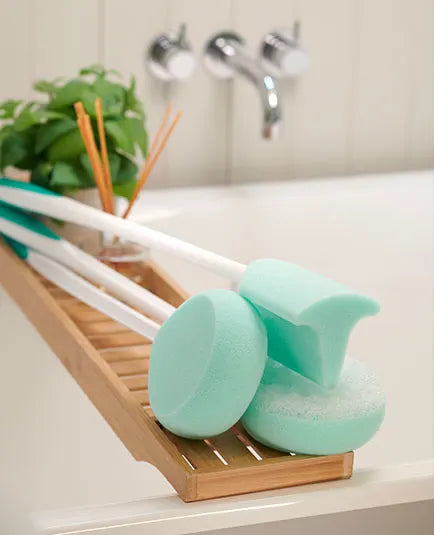 Two green sponges on a wooden dish rack with a bathroom setting in the background.