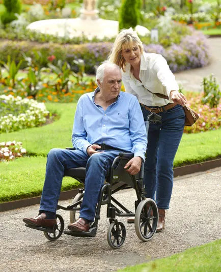 Man in a wheelchair being pushed by a woman in a garden setting