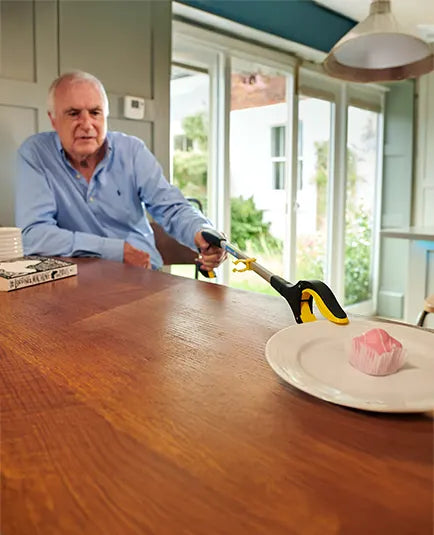 Man using a pair of tongs to pick up a pink object from a plate on a wooden table.