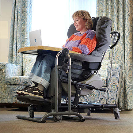 Person using a reclining chair with a laptop on a table attached to the chair in a home setting.