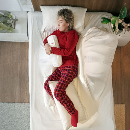 Person wearing red pajamas lying on a bed with a white pillow and bedding.
