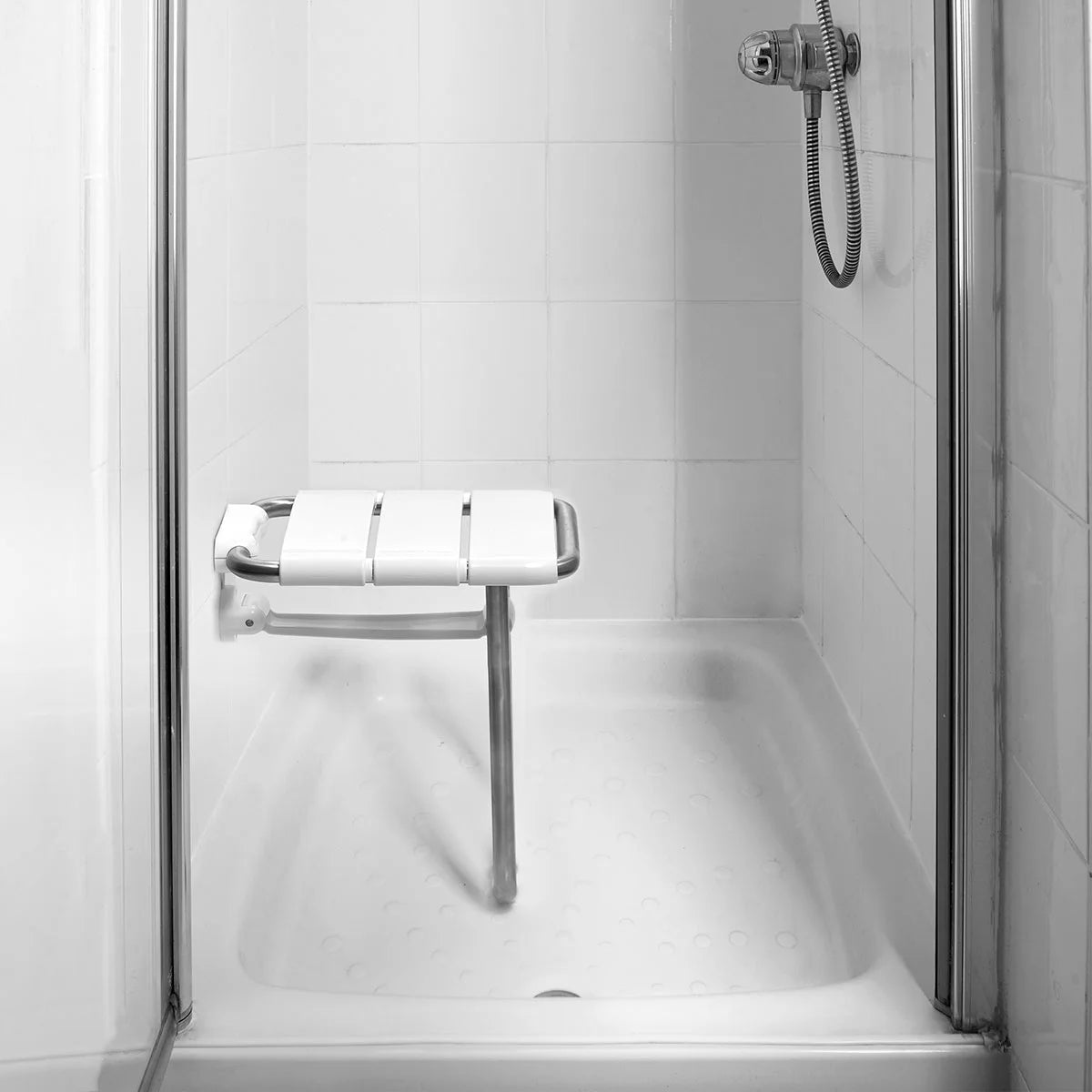Shower with a handheld shower head and shower seat in a tiled bathroom.