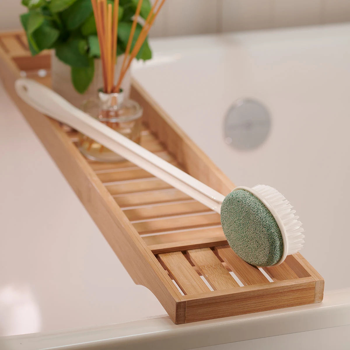 Bamboo bath caddy with scrub brush and sponge on a bathtub ledge.