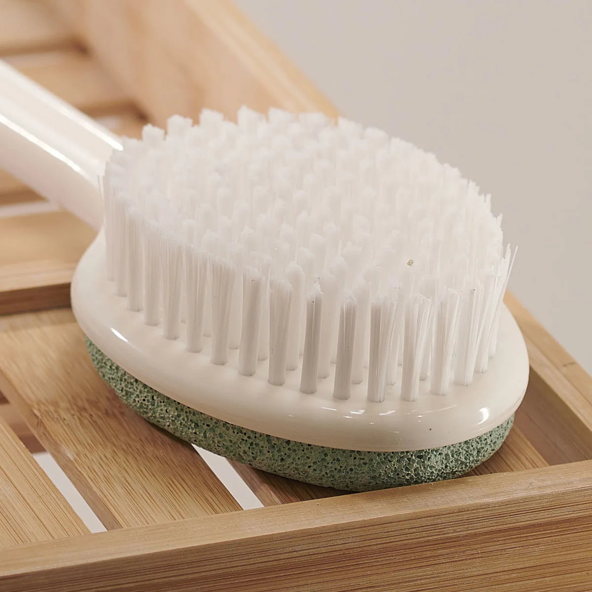 Cleaning brush with white bristles and green base on a wooden surface