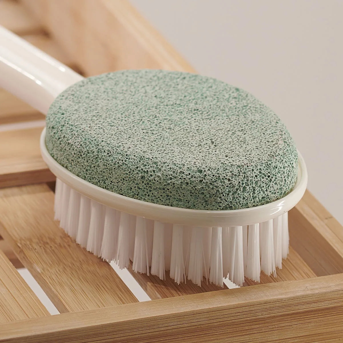 Cleaning brush with green sponge head on a wooden surface