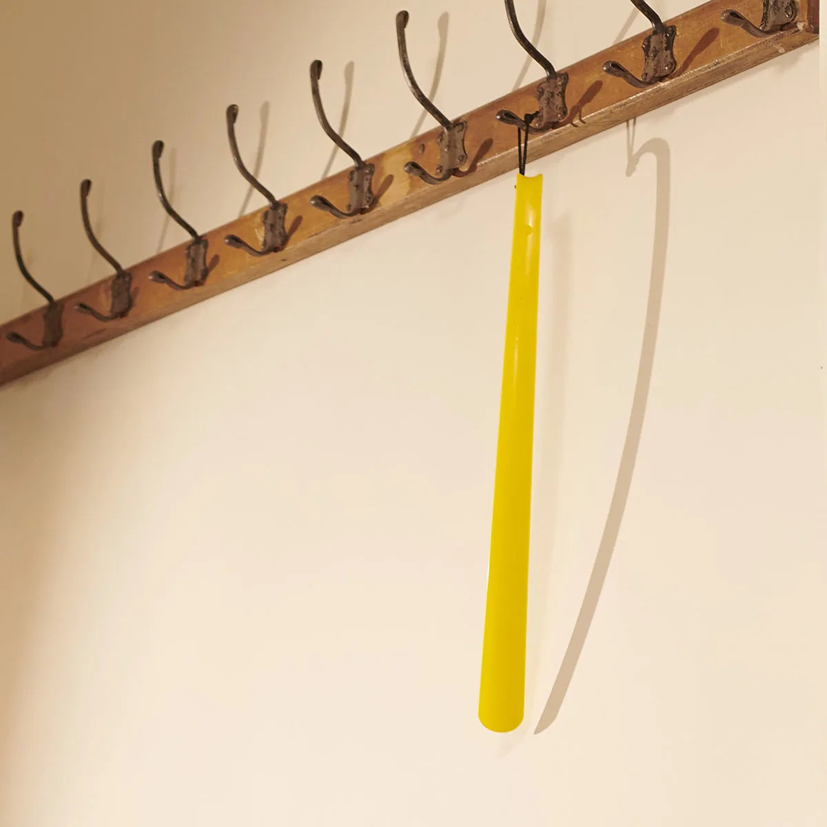 Yellow shoe horn hanging from a wooden peg rack on a beige wall.