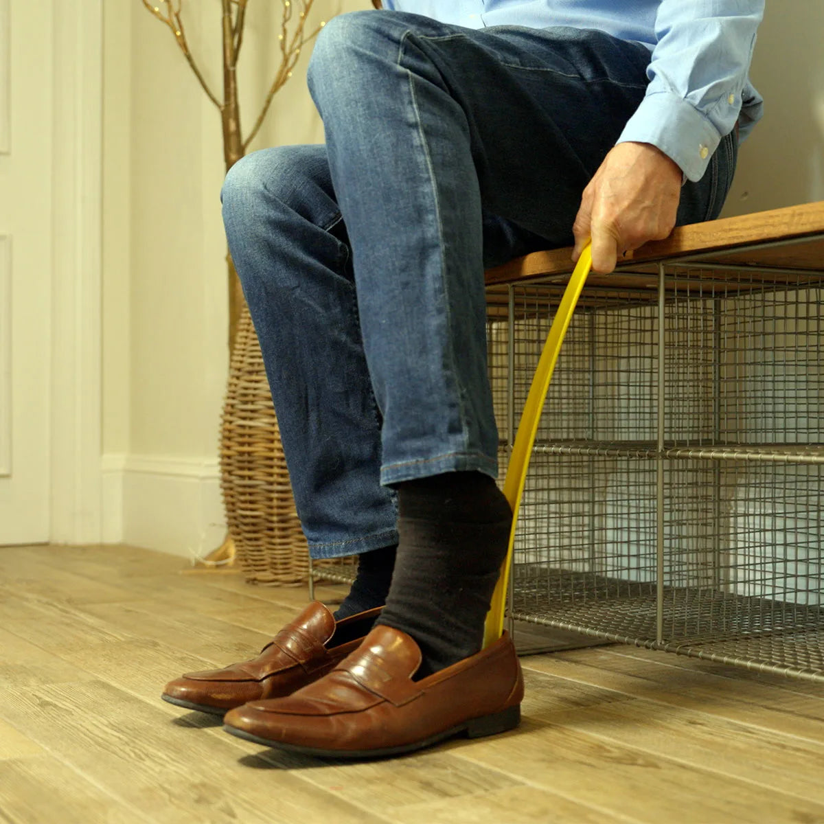 A person sitting on a bench using a yellow shoe horn to put on their shoes