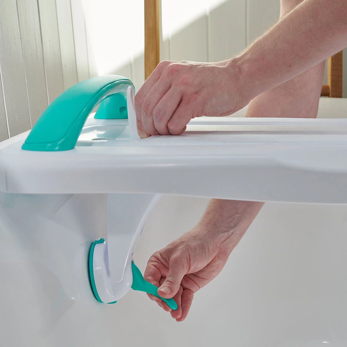 Person attaching a green bathtub support device on a white bathtub.