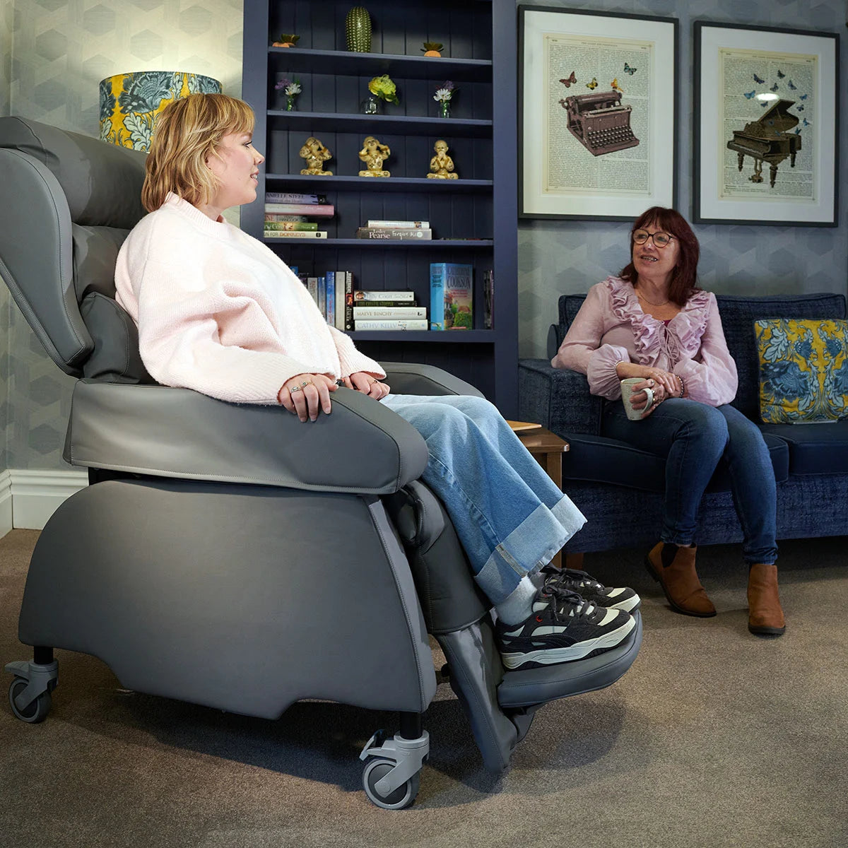 Woman using a reclining chair in a living room with another woman sitting on a couch.
