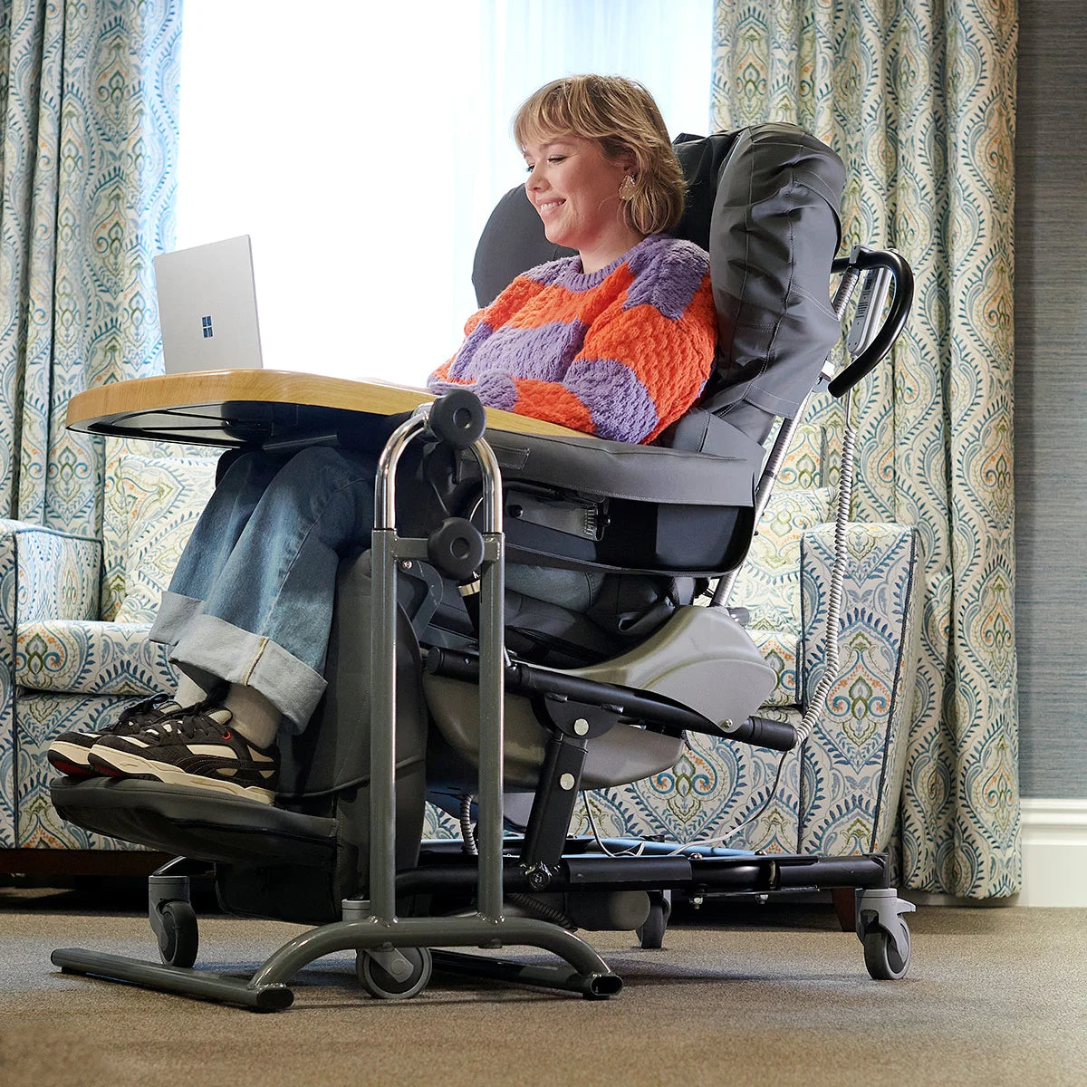 A person using a laptop in a grey reclining chair wearing a colourful jumper.