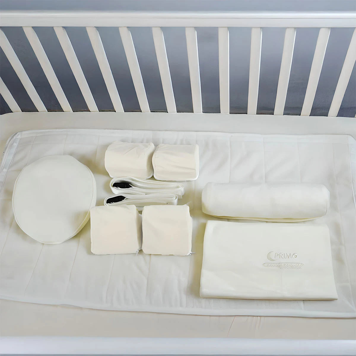 Baby crib with white bedding and accessories on a plain background