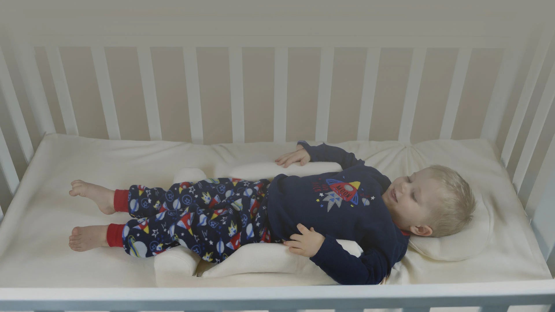 Child lying in a crib with a symmetry sleep wearing pyjamas with space-themed design.