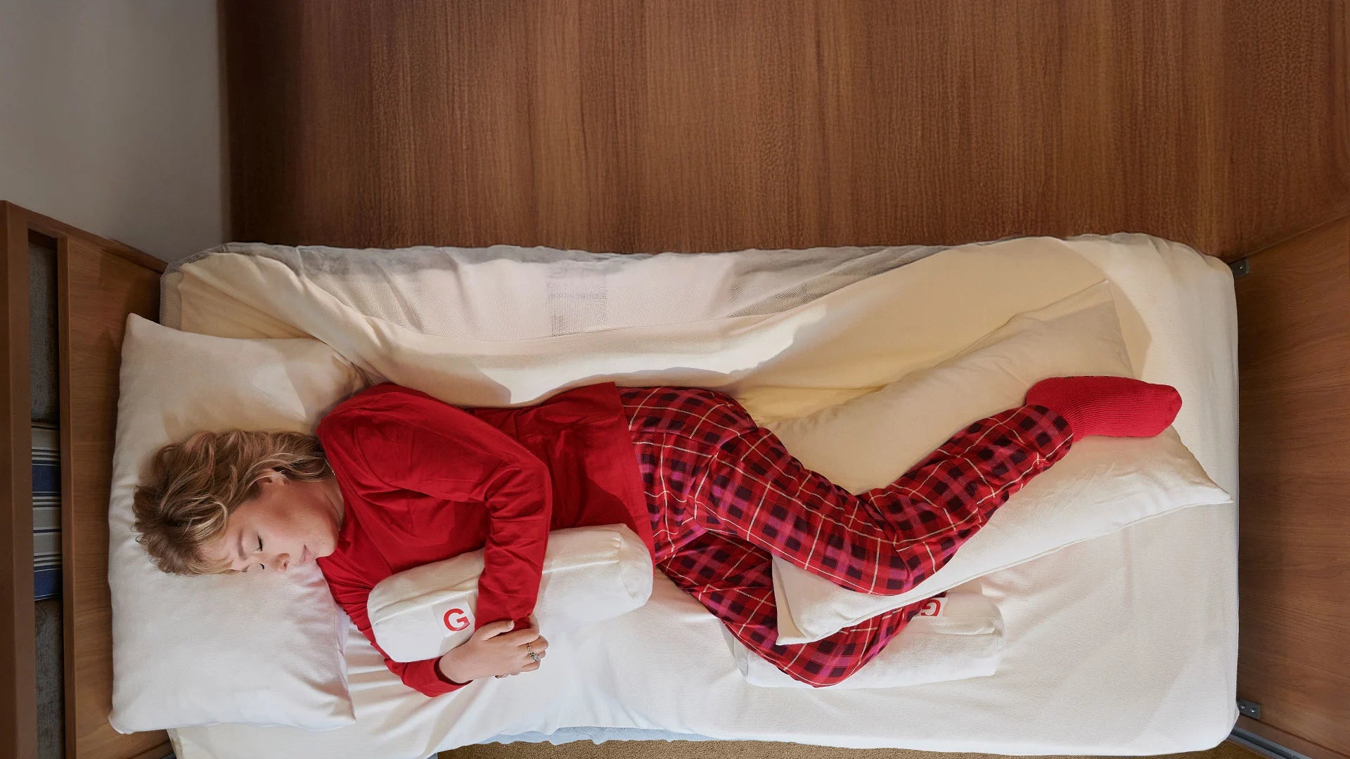 Person in red pyjamas lying in bed with a white supportive pillows and red socks.