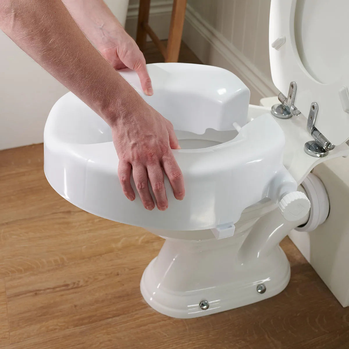 Person adjusting a raised toilet seat in a bathroom setting.