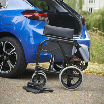 Black breezy manual wheelchair next to a blue car with grass and a house in the background