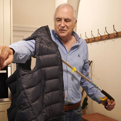 A man is using a pair of tongs to help him put on a black vest