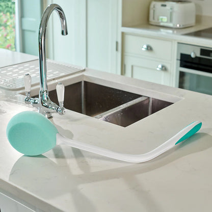 A teal bath sponge next to a kitchen sink