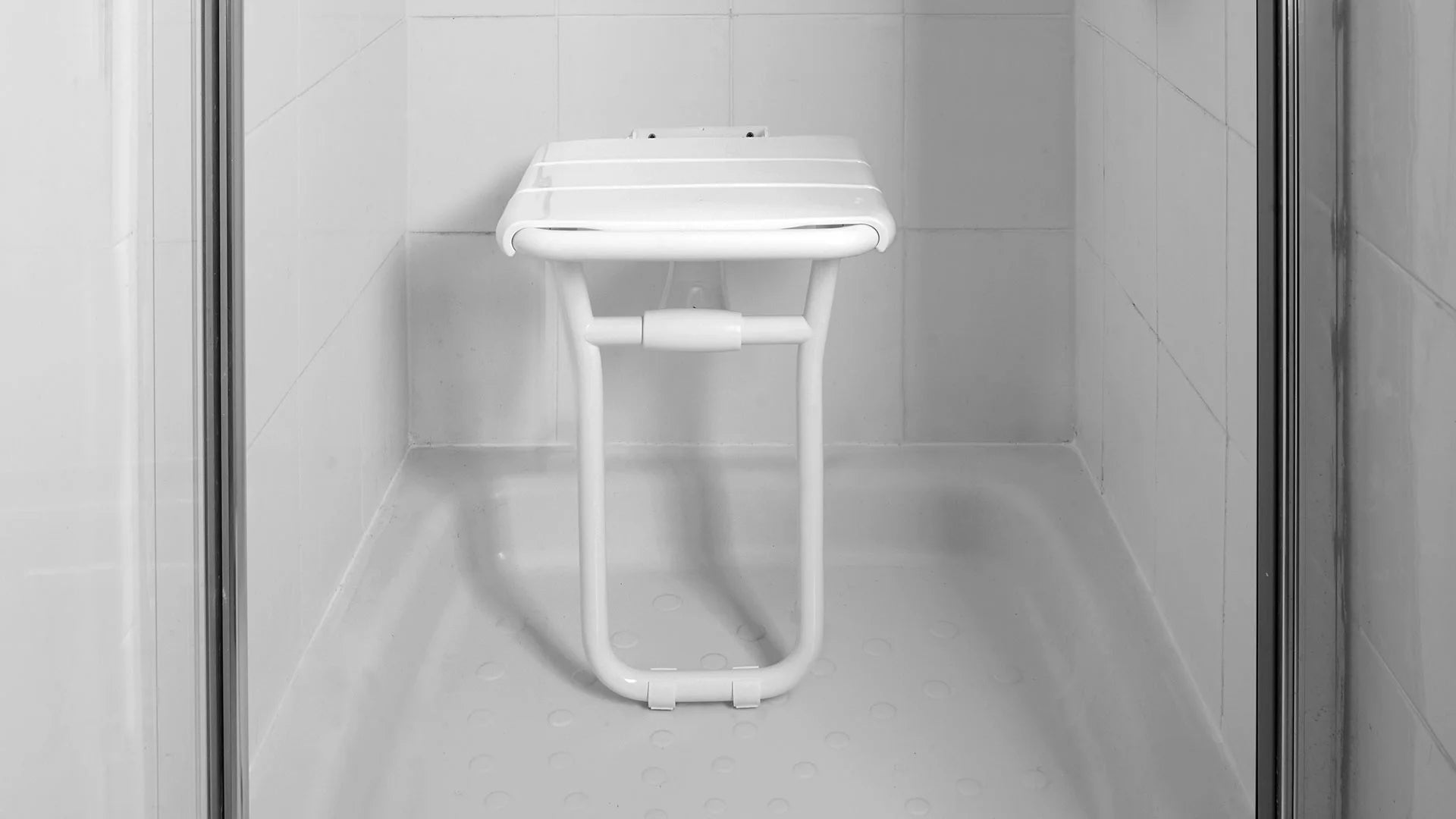 White shower seat mounted on a tiled wall in a shower enclosure.