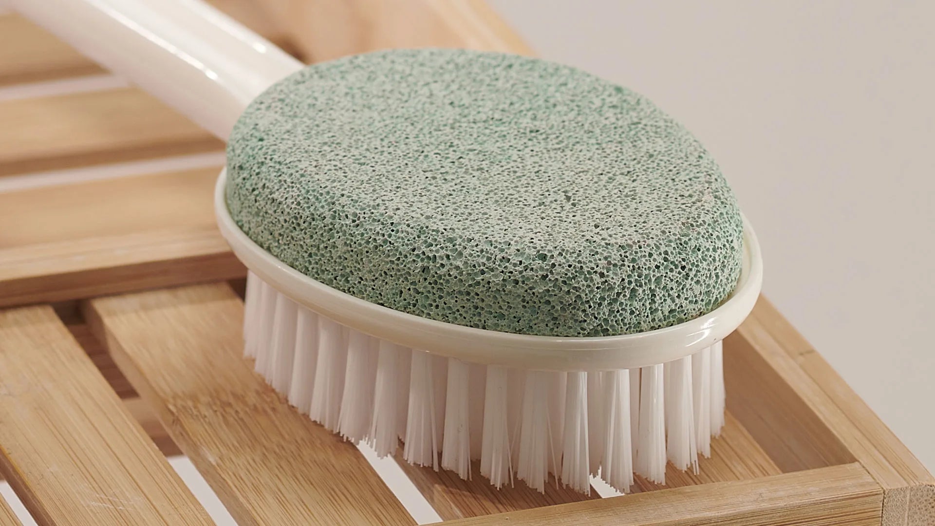 Green scrubbing brush with white bristles on a wooden surface